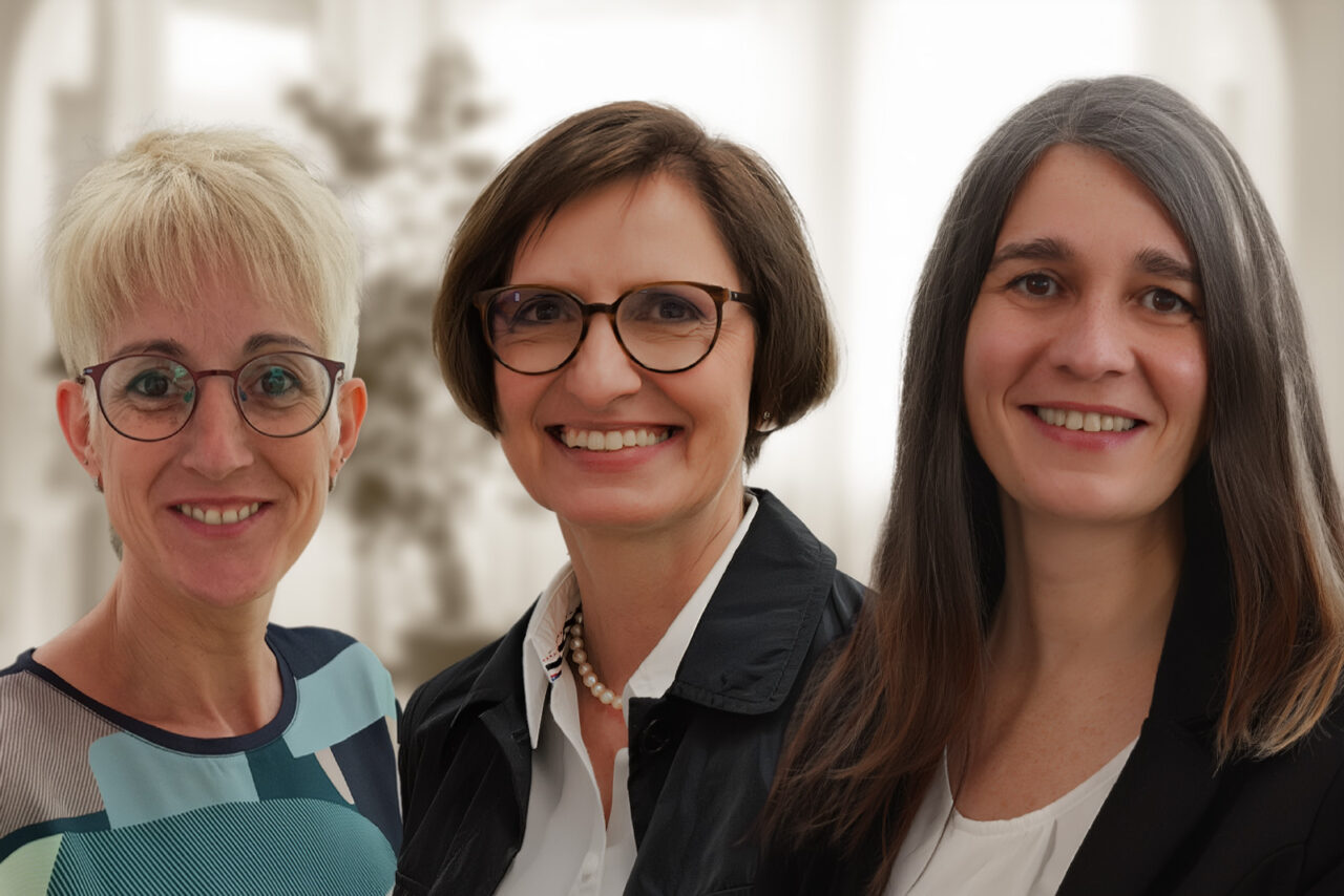 Drei Frauen vor einem Fenster blicken freundlich in die Kamera